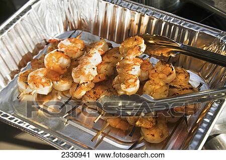 Stock Image - Barbequed shrimp skewers served in a foil pan; Canada. Fotosearch
