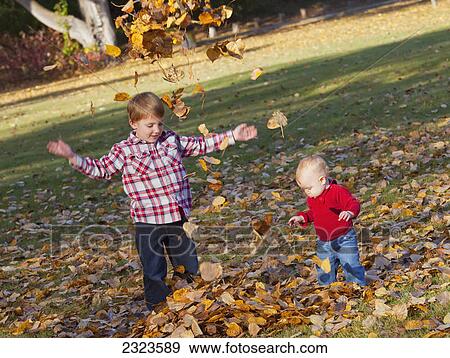 Stock Photo - Brother and sister playing in the leaves in a park in autumn; Edmonton alberta canada. Fotosearch