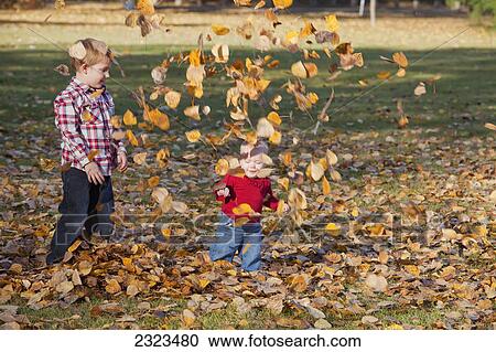 Stock Image - Brother and young sister play in the fallen leaves in a park in autumn; Edmonton alberta canada. Fotosearch