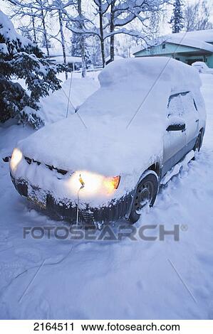 Stock Image - Car Covered In Fresh Blanket Of Snow From Storm With Lights On Winter Alaska. Fotosearch