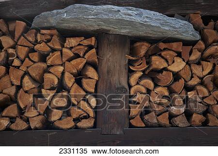 Stock Photography - Circular stone on top of wooden column with a pile of cut wood; Zermatt valais switzerland. Fotosearch