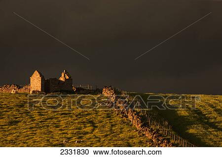 Stock Image - Dark storm clouds over building ruins and a stone fence along a field at sunset; Yorkshire dales england. Fotosearch