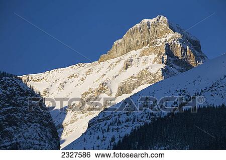 Early morning sunlight on snow covered mountain peak with deep blue sky; Lake louise alberta canada View Large Photo Image Stock Photograph - Early morning sunlight on snow covered mountain peak with deep blue sky; Lake louise alberta canada. Fotosearch