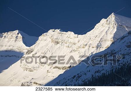 Early morning sunlight on snow covered mountain peaks with deep blue sky; Lake louise alberta canada View Large Photo Image Stock Photography - Early morning sunlight on snow covered mountain peaks with deep blue sky; Lake louise alberta canada. Fotosearch