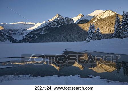Early morning sunlit snow covered mountains reflecting in a lake with deep blue sky; Lake louise alberta canada View Large Photo Image Picture - Early morning sunlit snow covered mountains reflecting in a lake with deep blue sky; Lake louise alberta canada. Fotosearch