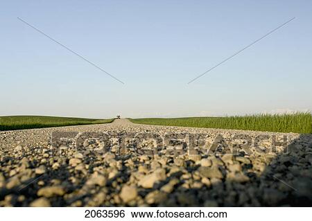 Stock Photograph - Extreme Low Angle Of Gravelled Country Road With Oncoming Vehicle; Canada, Manitoba, Erickson. Fotosearch