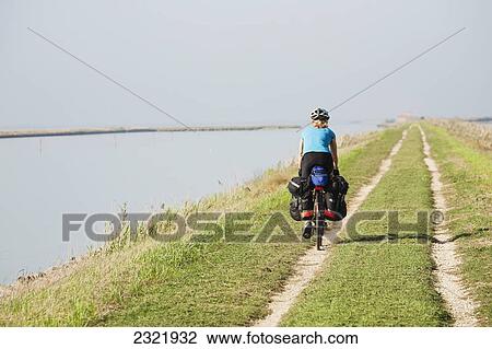 Female Cyclist On A Path Along A Body Of Water With Blue Sky; Comacchio Emilia-Romagna Italy View Large Photo Image Stock Image - Female Cyclist On A Path Along A Body Of Water With Blue Sky; Comacchio Emilia-Romagna Italy. Fotosearch