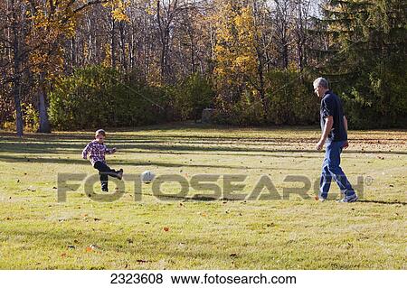 Stock Photo - Grandfather and grandson playing soccer in a park in autumn; Edmonton alberta canada. Fotosearch