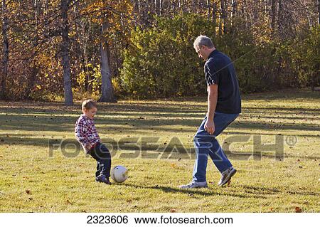 Stock Photograph - Grandfather and grandson playing soccer in a park in autumn; Edmonton alberta canada. Fotosearch