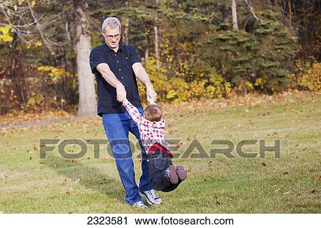 Stock Image - Grandfather swinging his grandson in a park in autumn; Edmonton alberta canada. Fotosearch