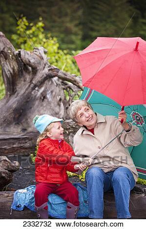 Grandmother and granddaughter playing with their umbrella while sitting on a log at the beach at Lowell Point on a rainy day, Summer, Seward, Southcentral Alaska, USA. View Large Photo Image Stock Image - Grandmother and granddaughter playing with their umbrella while sitting on a log at the beach at Lowell Point on a rainy day, Summer, Seward, Southcentral Alaska, USA.. Fotosearch