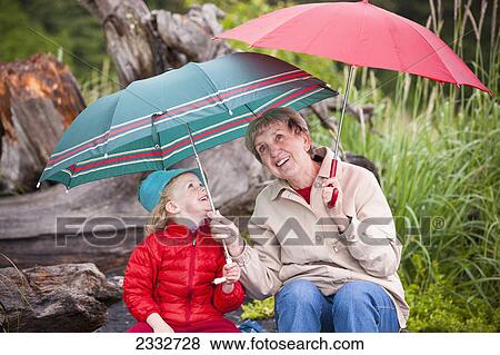 Grandmother and granddaughter playing with their umbrella while sitting on a log at the beach at Lowell Point on a rainy day, Summer, Seward, Southcentral Alaska, USA. View Large Photo Image Stock Photo - Grandmother and granddaughter playing with their umbrella while sitting on a log at the beach at Lowell Point on a rainy day, Summer, Seward, Southcentral Alaska, USA.. Fotosearch