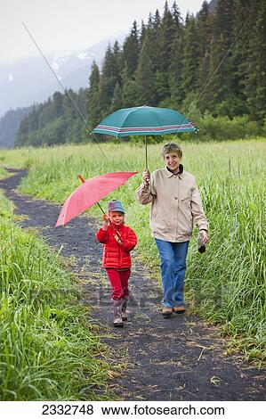 Grandmother and granddaughter playing with their umbrella while walking up the path from the beach at Lowell Point on a rainy day, summer, Seward, Southcentral Alaska, USA View Large Photo Image Stock Photo - Grandmother and granddaughter playing with their umbrella while walking up the path from the beach at Lowell Point on a rainy day, summer, Seward, Southcentral Alaska, USA. Fotosearch