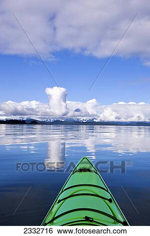 Stock Photograph - Green kayak on the tranquil water in lynn canal with the chilkat mountains in the distance; Alaska united states of america. Fotosearch