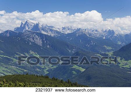 Stock Photo - Green Valleys With Tree-Filled Hills And Rocky Mountains With Cloud And Blue Sky; Bolzano Alto Adige Italy. Fotosearch
