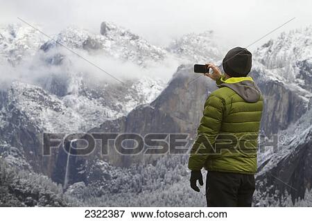Man wearing a green down jacket as seen from the back taking a picture of yosemite valley and bridal veil falls; Yosemite california united states of america View Large Photo Image Stock Photo - Man wearing a green down jacket as seen from the back taking a picture of yosemite valley and bridal veil falls; Yosemite california united states of america. Fotosearch