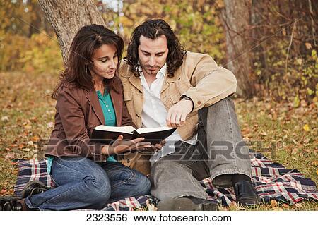 Stock Photograph - Married couple reading a bible in a park in autumn; Edmonton alberta canada. Fotosearch