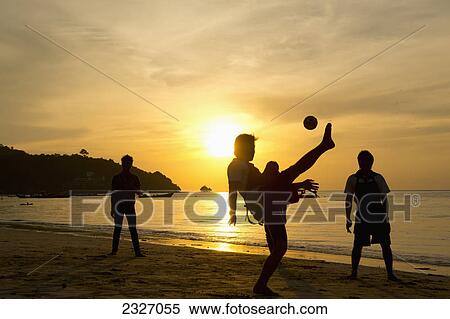 Stock Photography - Men playing takraw ball at sunset on the beach; Phuket thailand. Fotosearch