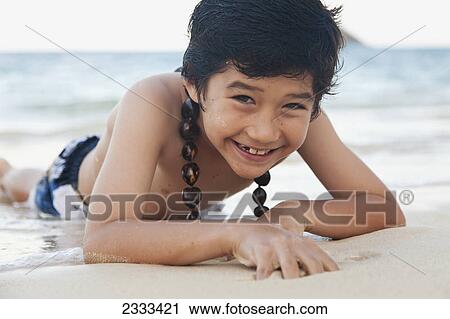 Stock Image - Portrait of a boy laying at the water's edge on the beach; Honolulu hawaii united states of america. Fotosearch