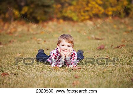 Portrait of a young boy laying in the grass in a park in autumn; Edmonton alberta canada View Large Photo Image Stock Image - Portrait of a young boy laying in the grass in a park in autumn; Edmonton alberta canada. Fotosearch