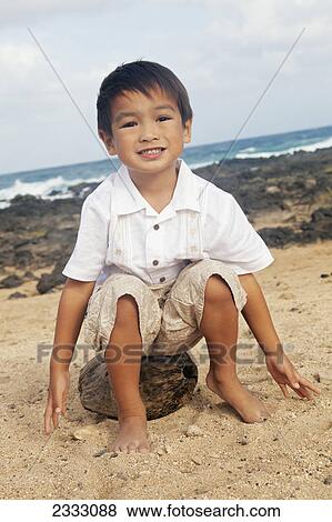 Portrait of a young boy sitting on a coconut on the sand at the water's edge; Honolulu oahu hawaii united states of america View Large Photo Image Stock Photo - Portrait of a young boy sitting on a coconut on the sand at the water's edge; Honolulu oahu hawaii united states of america. Fotosearch