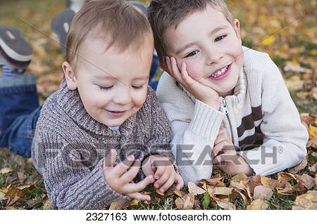 Stock Image - Portrait of two young boys laying on fallen leaves in autumn colours; St. albert alberta canada. Fotosearch