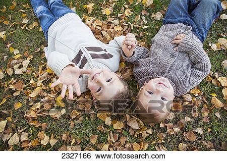 Portrait of two young boys laying on fallen leaves in autumn colours; St. albert alberta canada View Large Photo Image Stock Photograph - Portrait of two young boys laying on fallen leaves in autumn colours; St. albert alberta canada. Fotosearch