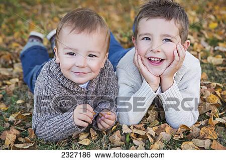 Stock Photograph - Portrait of two young boys laying on the ground in fallen autumn leaves; St. albert alberta canada. Fotosearch