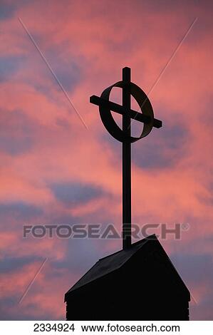 Picture - Silhouette of a cross on church steeple with fiery cloud cover in the sky at sunrise; Calgary alberta canada. Fotosearch