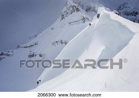 Stock Image - Skier On Crest Of Big Drop, Dwarfed By Mountain; Canada, British Columbia, Icefall Lodge. Fotosearch