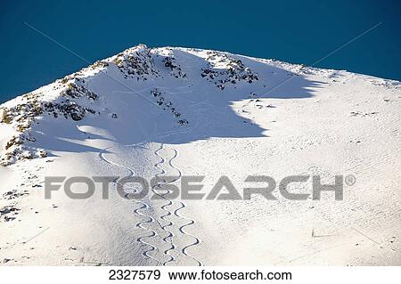 Stock Photo - Snow covered mountain peak with skier tracks and deep blue sky; Lake louise alberta canada. Fotosearch