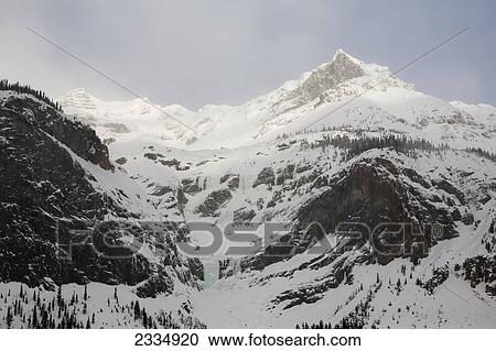 Snow covered mountains with the sun highlighting the peaks and a hazy blue sky; Field alberta canada View Large Photo Image Stock Image - Snow covered mountains with the sun highlighting the peaks and a hazy blue sky; Field alberta canada. Fotosearch