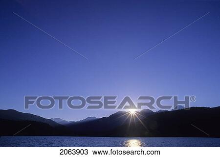Stock Image - Sunburst Over Mountains At Dawn, Green Lake At Whistler, Bc. Fotosearch