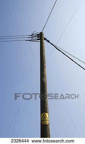 Picture - Telephone and electricity cables and post against a blue sky; England. Fotosearch