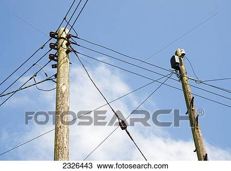 Stock Image - Telephone and electricity cables against a blue sky and cloud; England. Fotosearch
