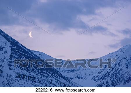 Stock Photograph - The crescent moon sets above the sentinel range along the alaska highway muncho lake provincial park northern canadian rockies; British columbia canada. Fotosearch