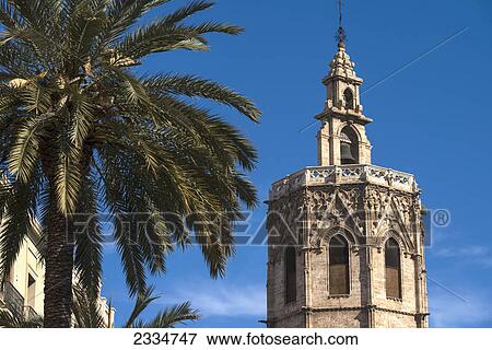 Stock Photo - The Miguelete, the tower of the Cathedral of Valencia above palm trees and buildings of Plaza de la Reina; Valencia, Spain. Fotosearch