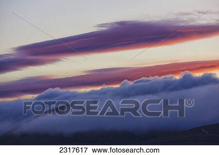 Stock Photo - The Morning Light Illuminates Clouds Above The Mist Covering Richardson Mountains Along The Dempster Highway; Yukon Canada. Fotosearch