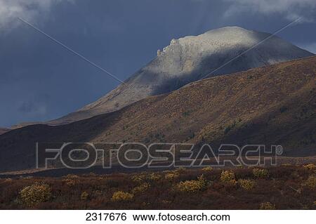 Stock Photograph - The Mountains Along The Dempster Highway Are Illuminated In Dramatic Storm Light As The Clouds Break; Yukon Canada. Fotosearch