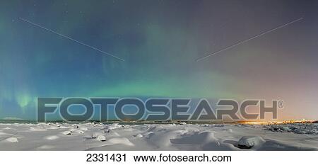 Stock Image - The northern lights shine above the anchorage city skyline in this nighttime view from the tony knowles coastal trail in winter; Anchorage alaska united states of america. Fotosearch