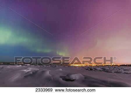 Stock Photo - The Northern Lights shine above the Anchorage city skyline in this nighttime view from the Tony Knowles Coastal Trail in winter; Anchorage, Alaska, United States of America. Fotosearch