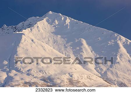 Stock Image - The setting sun highlights the ridgeline and cornices on Lark Mountain, Chugach National Forest, Winter, Moose Pass, Southcentral Alaska, USA.. Fotosearch