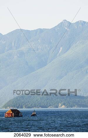 Stock Photo - Tug Boat Pulling Logs Through The Ocean With Mountains In The Background, Howe Sound, Bc. Fotosearch