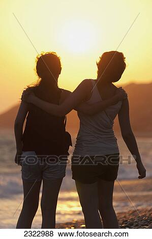 Two friends in an embrace as they watch the sunset at the water's edge; Aphrodite bay cyprus View Large Photo Image Stock Photo - Two friends in an embrace as they watch the sunset at the water's edge; Aphrodite bay cyprus. Fotosearch