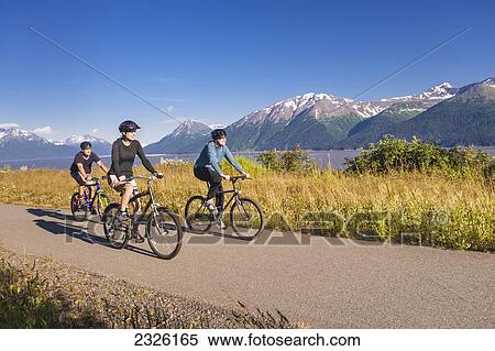 Stock Photography - Two women and a man biking on the bird point to girdwood bike trail turnagain arm; Anchorage alaska united states of america. Fotosearch