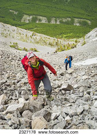 Stock Photo - Two young women climbing scree to a cave entrance; Crowsnest pass alberta canada. Fotosearch