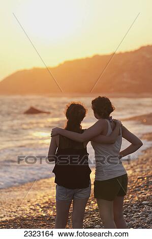 Two young women in an embrace watch the sunset while looking out over the ocean; Aphrodite bay cyprus View Large Photo Image Picture - Two young women in an embrace watch the sunset while looking out over the ocean; Aphrodite bay cyprus. Fotosearch