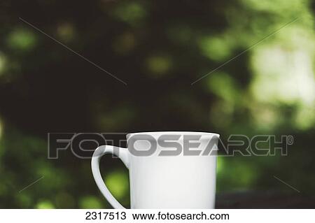 Stock Image - White Coffee Mug Against A Green Forest Background; Thedford Mines Quebec Canada. Fotosearch