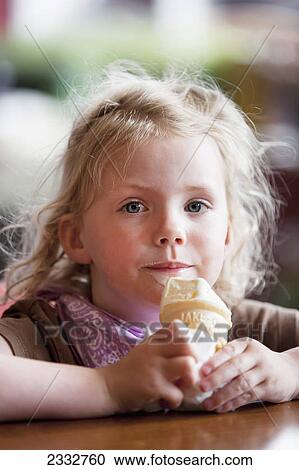 Stock Image - Young girl eating a ice cream cone while sitting in a coffe shop on a rainy day in Seward, summer, Seward, Southcentral Alaska, USA. Fotosearch