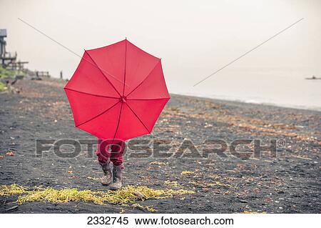 Stock Photography - Young girl playing with her red umbrella while walking on the beach at Lowell Point on a rainy day, summer, Seward, Southcentral Alaska, USA. Fotosearch
